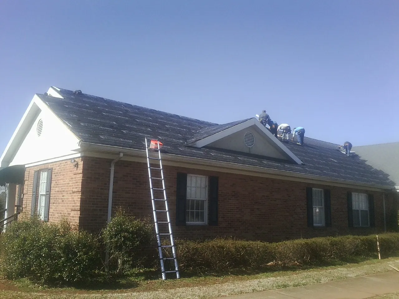 Crew tearing shingles off a brick ranch roof with a ladder set — Emergency Roof Repair work by our crew in Brownsville