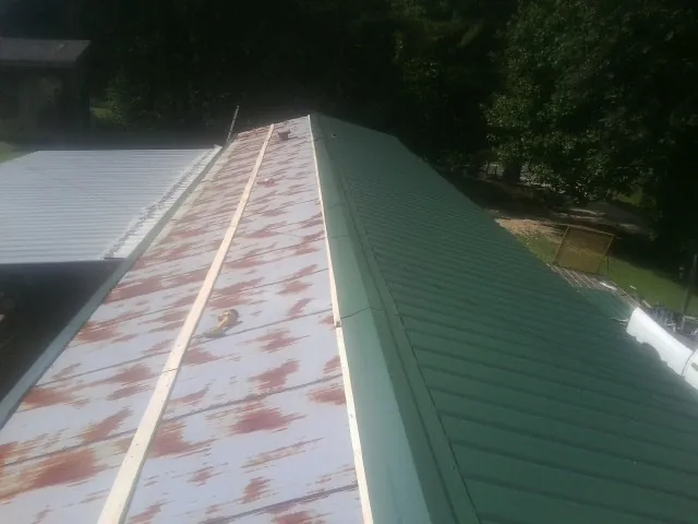 Old rusted panels beside newly installed green metal roofing — Wind Damage Roof Repair by Roofing Brothers in Brownsville